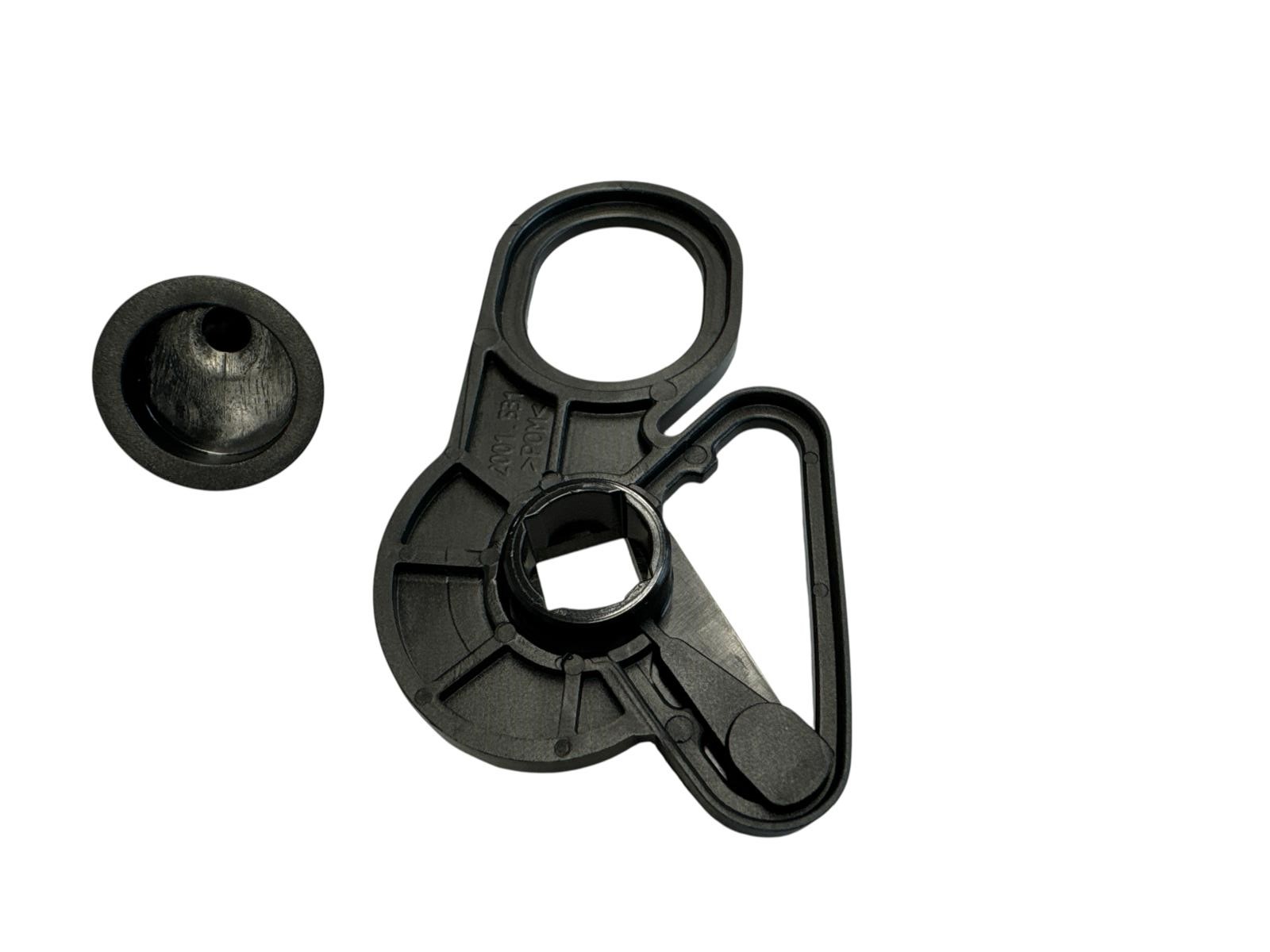 Das Bild zeigt zwei schwarze Kunststoffteile auf einem weißen Hintergrund. Ein Teil ist ein kleiner, zylindrischer Knopf mit einem quadratischen Kopf. Das andere Teil ist größer und komplexer geformt, mit einem Loch, einem Haken und einer quadratischen Öf