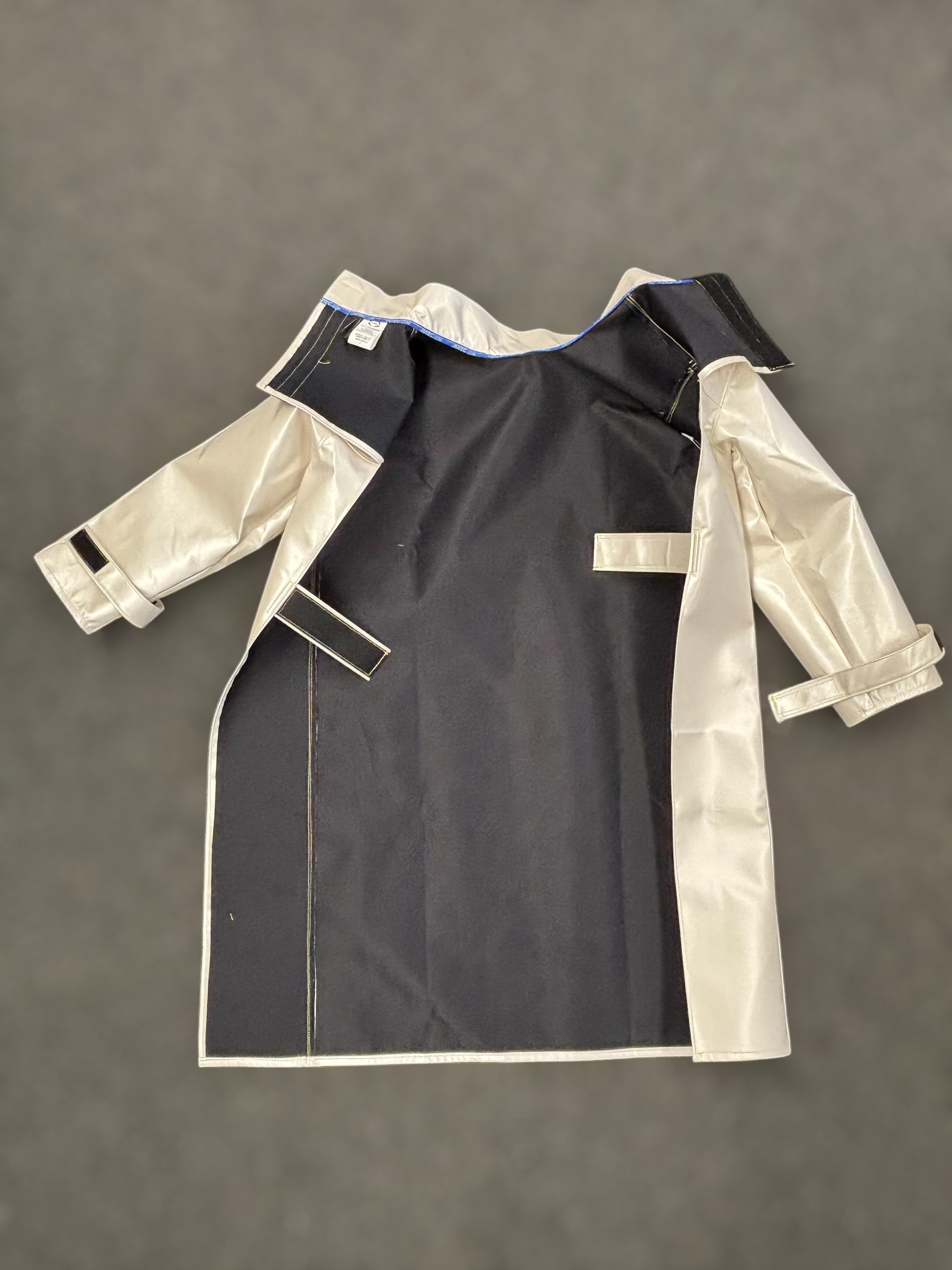 Laserschutzmantel mit schwarzer Innenseite und hellen Ärmeln liegend auf grauem Untergrund