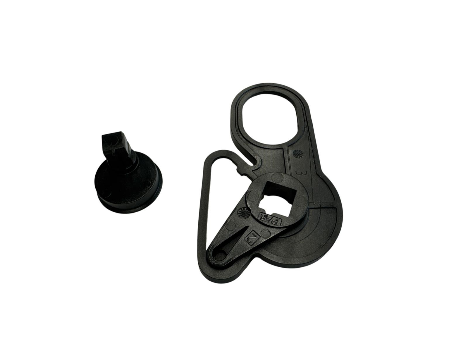 Das Bild zeigt zwei schwarze Kunststoffteile auf einem weißen Hintergrund. Ein Teil ist ein kleiner, zylindrischer Knopf mit einem quadratischen Kopf. Das andere Teil ist größer und komplexer geformt, mit einem Loch, einem Haken und einer quadratischen Öf