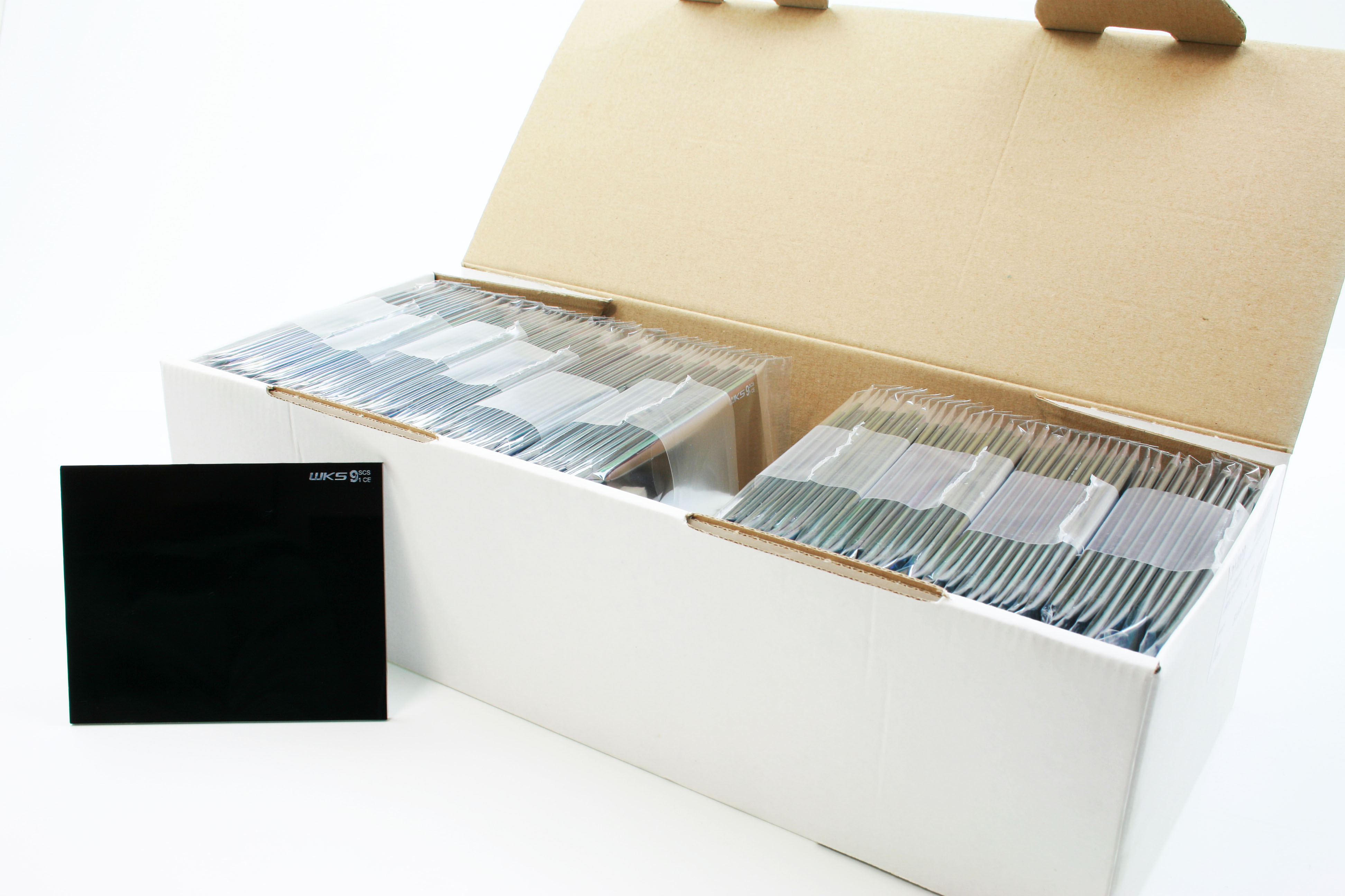 Offene weiße Verpackung mit mehreren Stapeln schwarzer Schweißelektroden in Folie verpackt, eine Elektrode steht davor mit Aufdruck 'WKS 9 3/16'