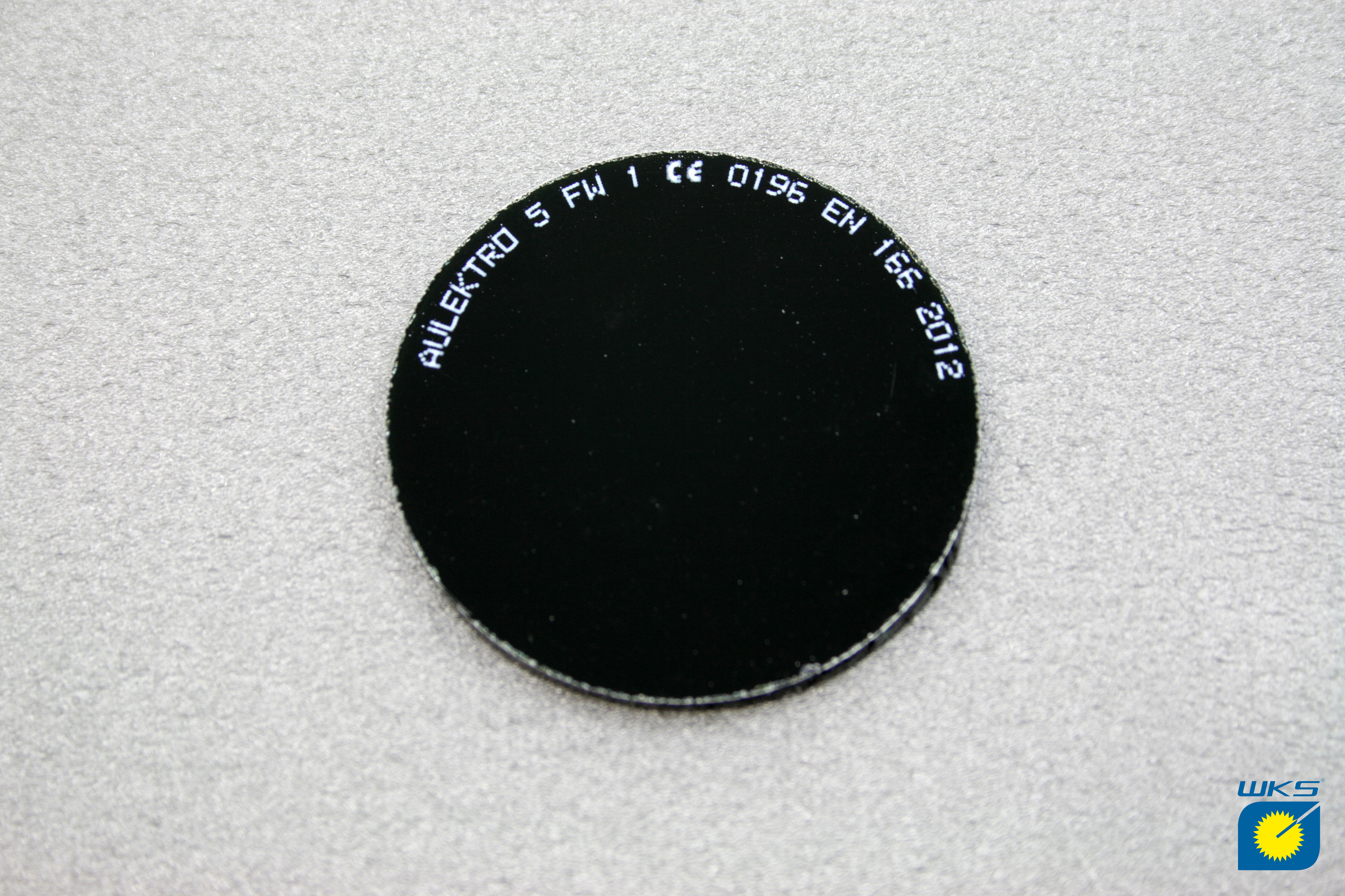 Rundes schwarzes Schweißfilterglas mit der Aufschrift 'AULEKTRO 5 FW 1 CE 0195 EN 166 2012' auf grauem Hintergrund